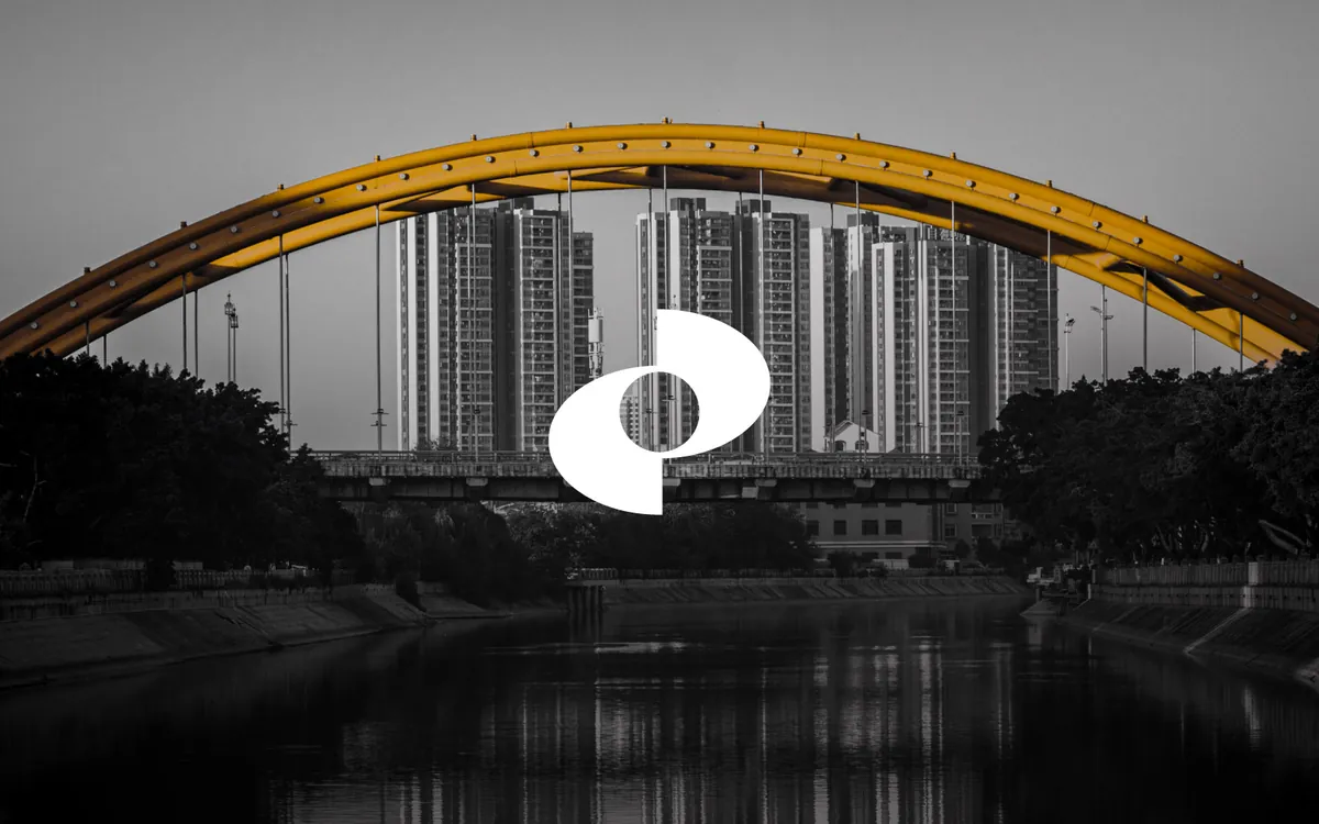 Il simbolo Bridge$ in bianco su una fotografia in bianco e nero di un ponte ad arco, con l’arcata in arancione