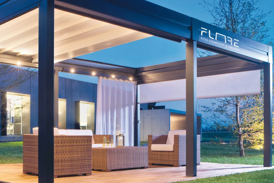 Il logotipo Flare in bianco sulla trave di una pergola al crepuscolo, con divani e luci accese